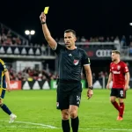 MLS-Schiedsrichter hält eine gelbe Karte hoch, im Hintergrund unscharfe Spieler